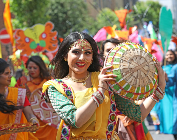 Woman in traditional South Asian dress holding a colorful woven basket during a cultural street parade