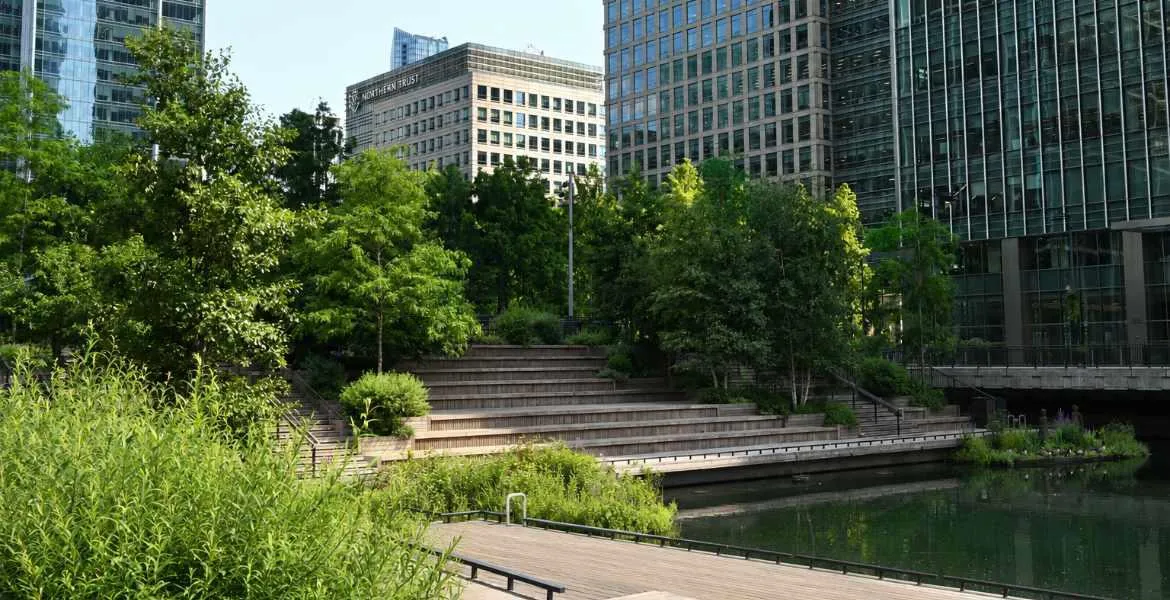 Landscaped garden with a pond, wooden terraces and lush planting, surrounded by modern office towers in Canary Wharf.