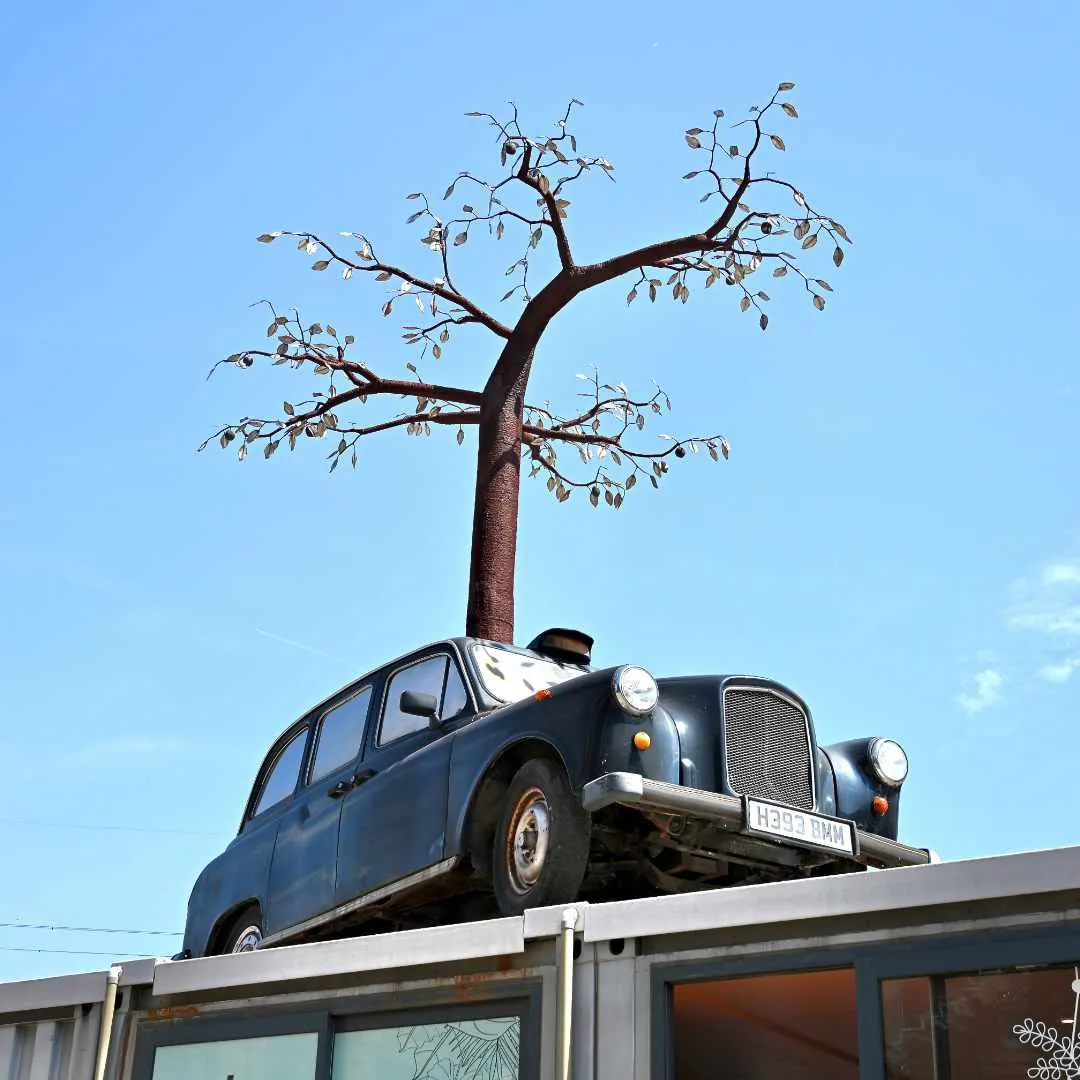Vintage black cab mounted on a rooftop beneath a metal tree sculpture, set against a clear blue sky at Trinity Buoy Wharf
